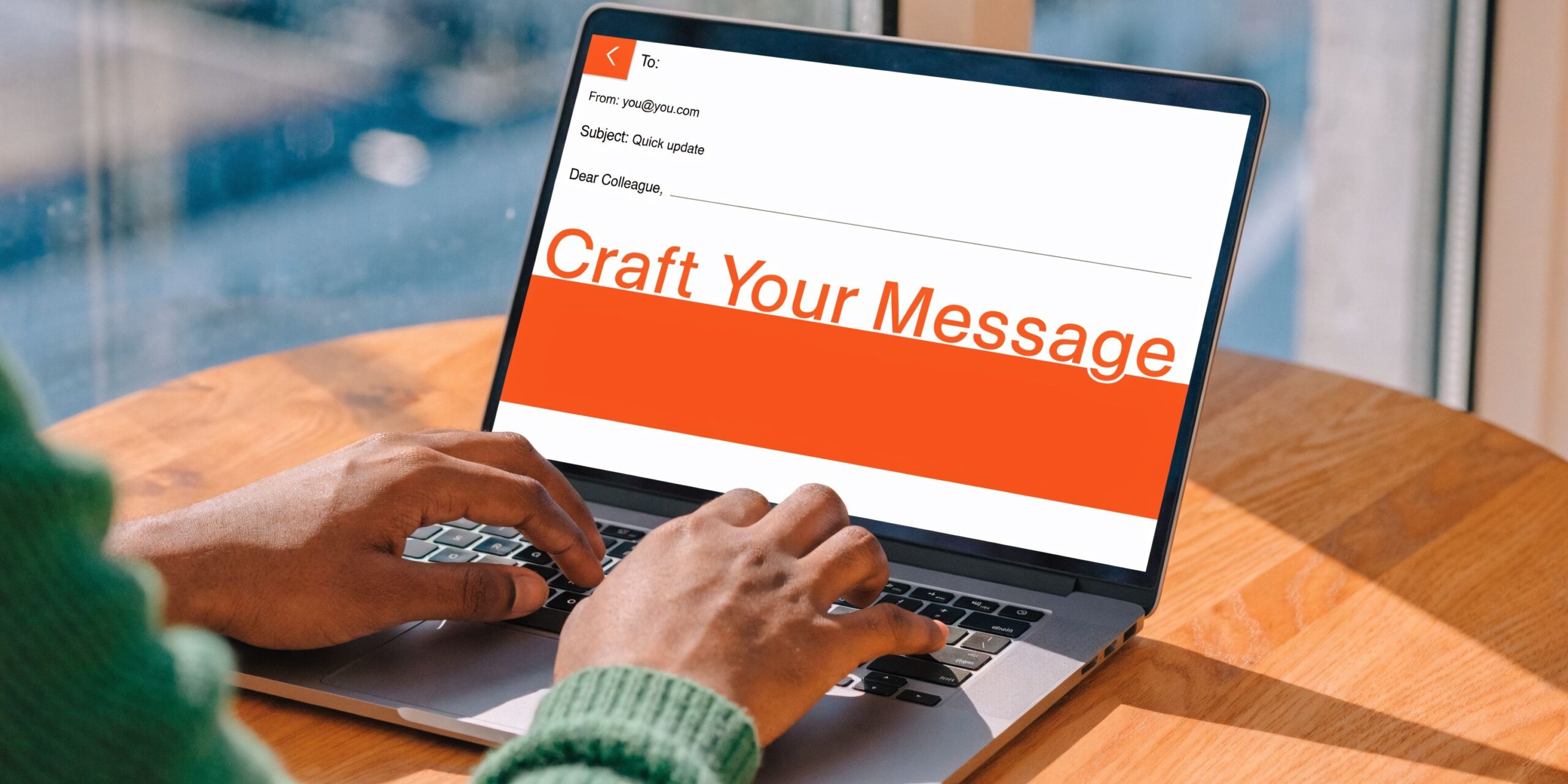 A person typing on a laptop computer screen displaying a message crafting interface on a wooden table.