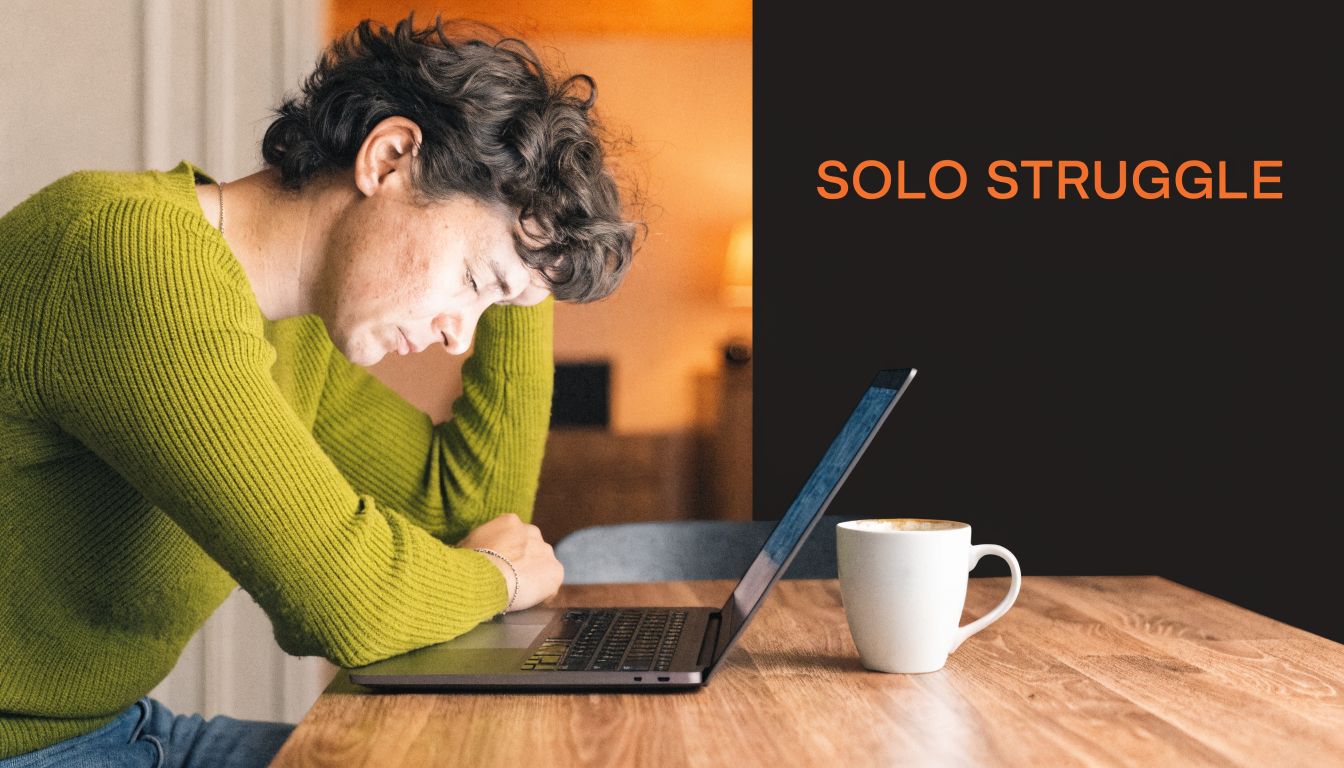 A person sitting at a desk with a laptop looking stressed and tired while working alone.