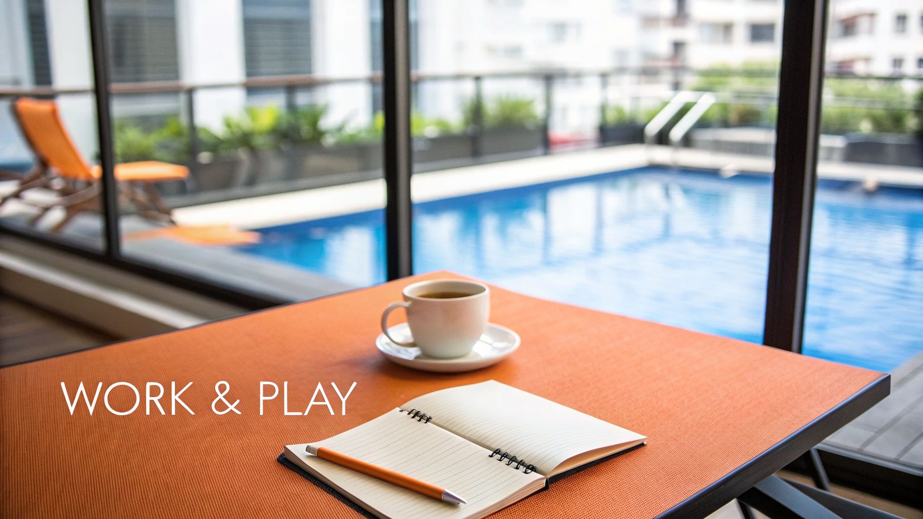 A vibrant orange table with a coffee cup and notebook overlooking a sunny swimming pool.