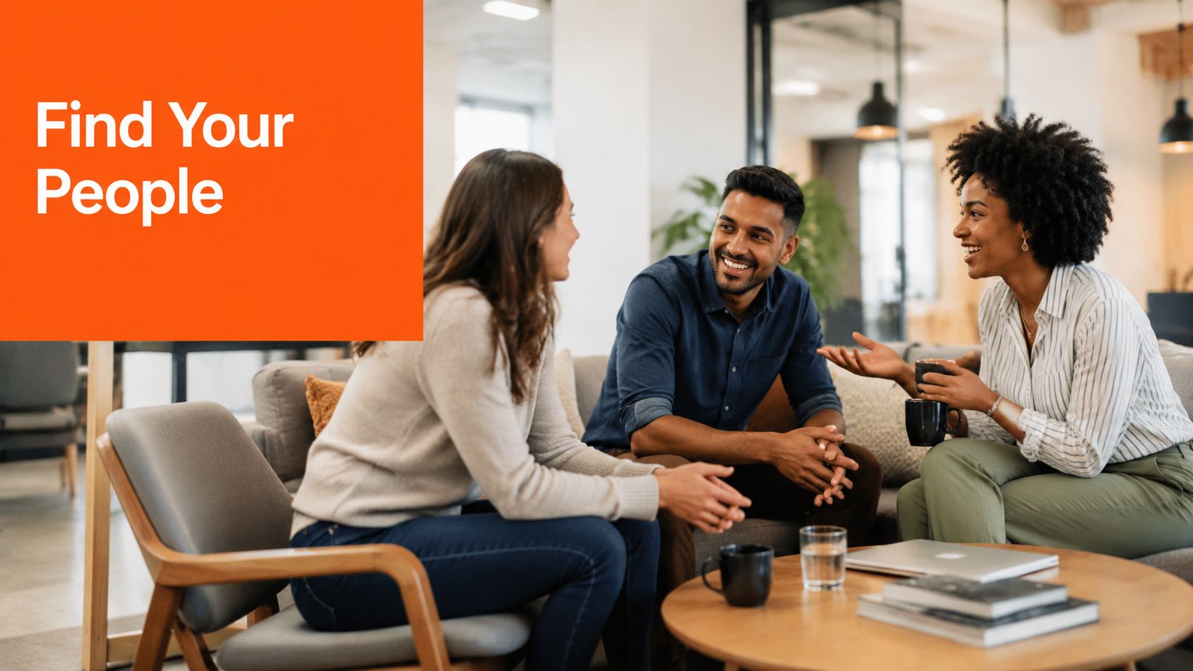 Three diverse colleagues smiling and chatting together while sitting on a comfortable couch in a modern office.