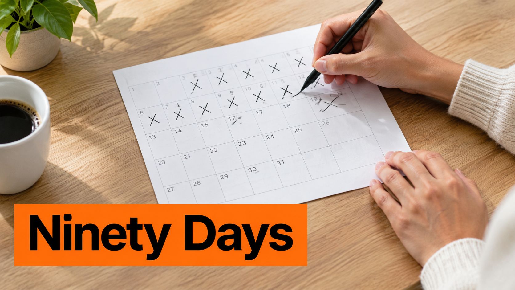 A person marks off days on a paper calendar with a black pen on a wooden desk.